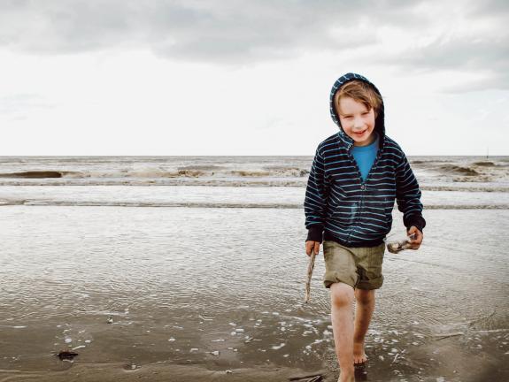 Auf dem 14 Kilometer langen Sandstrand lässt sich es herrlich Toben, Buddeln und Baden. Junge am Strand beim Muschelsammeln
