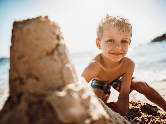 Sandburgenbauen als generationenübergreifende Baukultur fördert Kreativität und familiären Teamgeist. Kind beim Sandburgenbauen am Strand