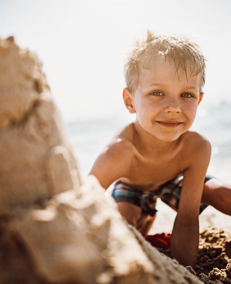 Unschlagbare Kombi: Sand, Sonne, Meer Junge baut Sandburg